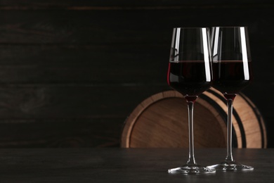 Glasses of red wine and wooden barrel on background. Space for text