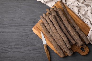Photo of Raw salsify roots and knife on grey wooden table, top view. Space for text