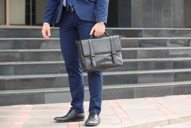 Businessman with black briefcase in hand outdoors. Space for text