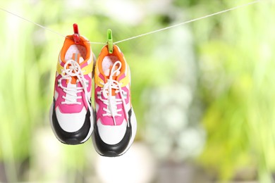 Stylish sneakers drying on washing line against blurred background, space for text