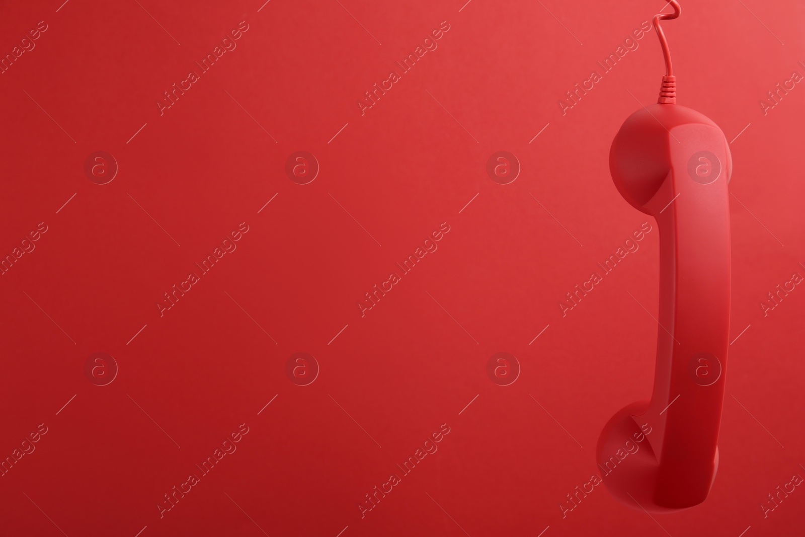 Photo of Corded telephone handset hanging on red background, space for text. Hotline concept