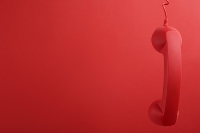 Corded telephone handset hanging on red background, space for text. Hotline concept