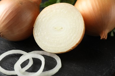 Photo of Whole and cut onions on black textured table, closeup