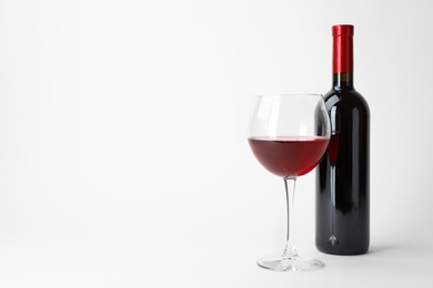 Photo of Bottle and glass of expensive red wine on light background