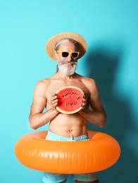 Shirtless man with inflatable ring and watermelon on color background