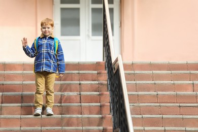 Photo of Cute boy with backpack standing near school