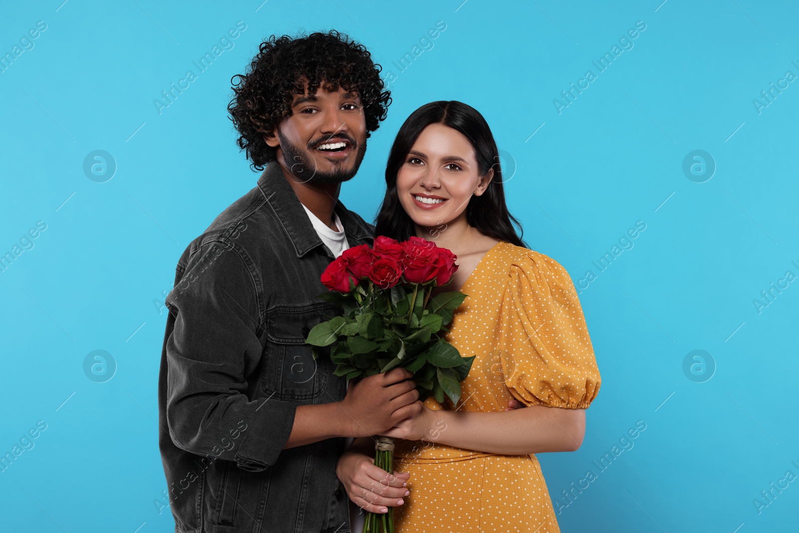 Photo of International dating. Happy couple with bouquet of roses on light blue background