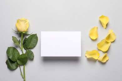 Beautiful yellow rose, petals and blank card on light grey background, flat lay. Space for text