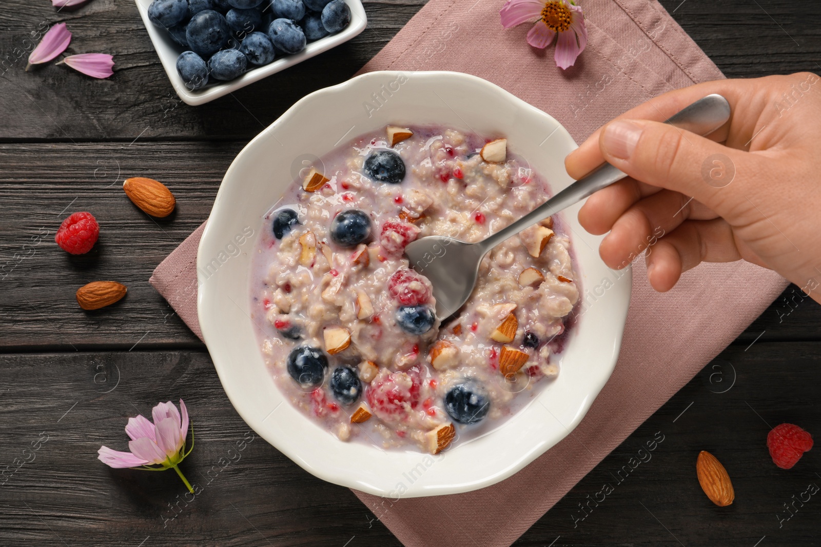 Photo of Woman eating tasty oatmeal porridge with toppings at black wooden table, top view