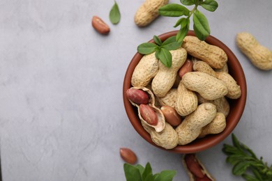 Photo of Fresh unpeeled peanuts in bowl and leaves on grey table, flat lay. Space for text