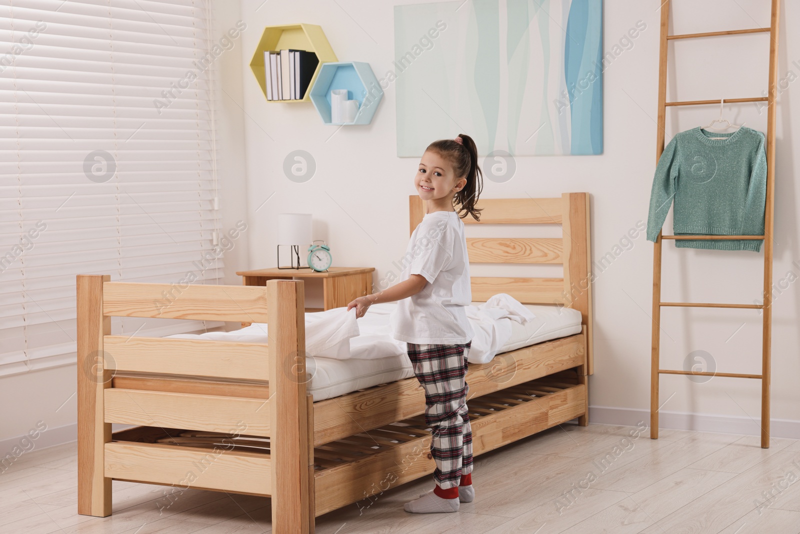 Photo of Cute girl changing bed linens in children room