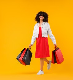 Photo of Happy young woman with shopping bags and stylish sunglasses on yellow background. Space for text