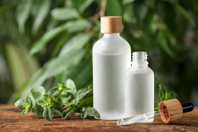 Photo of Bottles of mint essential oil and fresh leaves on wooden table against blurred background, space for text