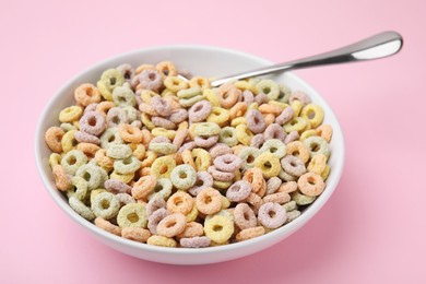 Photo of Tasty cereal rings in bowl and spoon on pink table, closeup