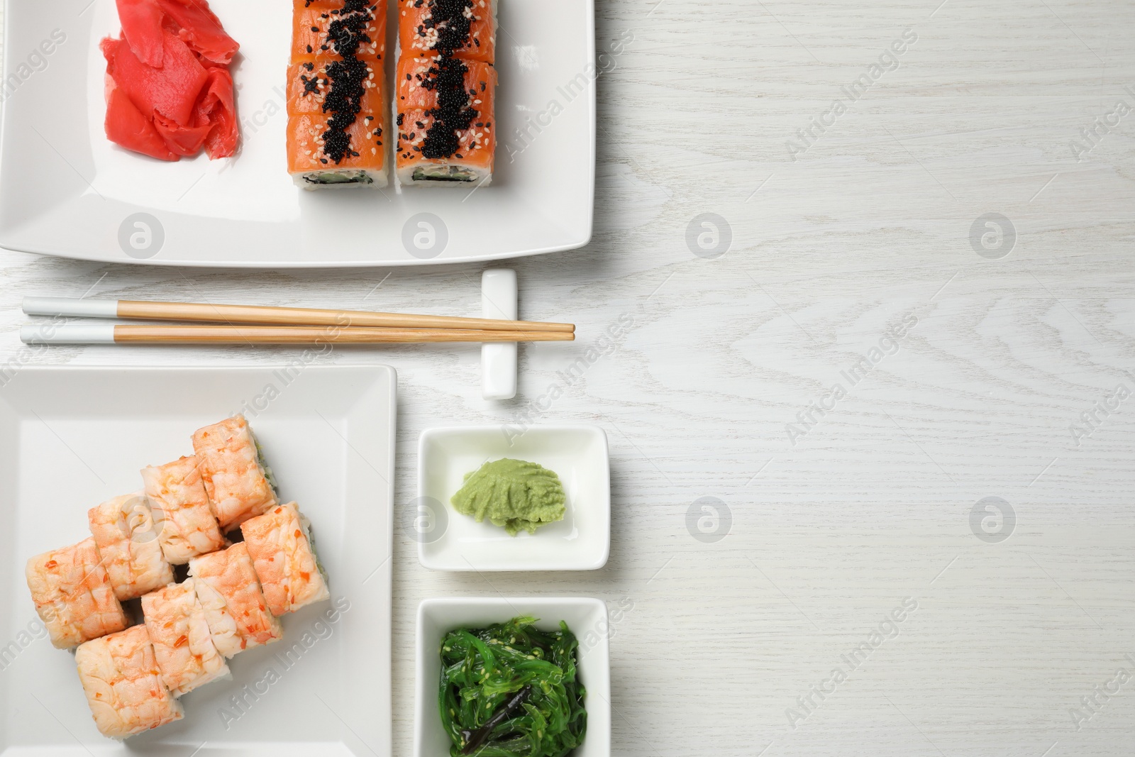 Photo of Delicious sushi rolls served on white wooden table, flat lay. Space for text