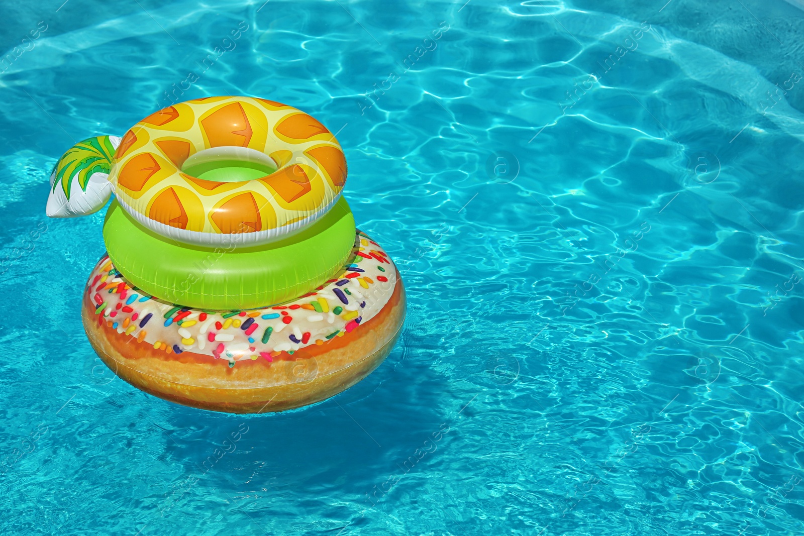 Photo of Stack of colorful inflatable rings floating in swimming pool on sunny day. Space for text