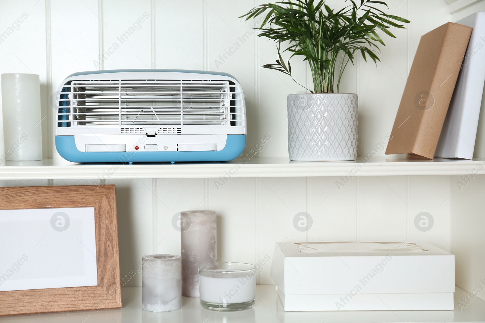 Photo of Modern air purifier and different items on white wooden shelves