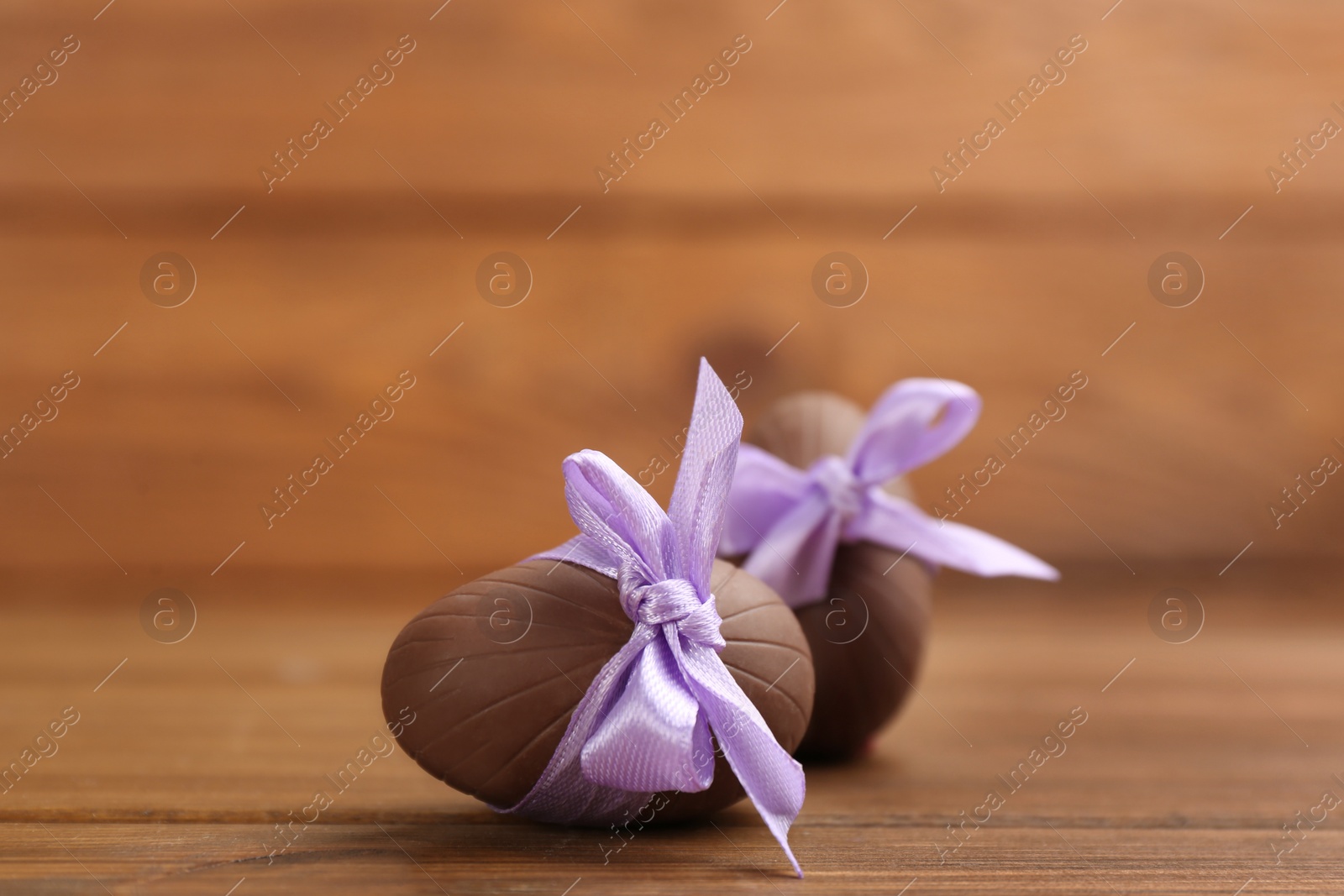 Photo of Sweet chocolate eggs with violet bows on wooden table. Space for text