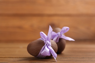 Sweet chocolate eggs with violet bows on wooden table. Space for text