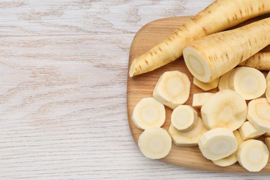Photo of Whole and cut fresh ripe parsnips on white wooden table, top view. Space for text