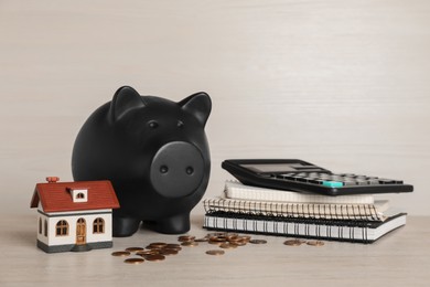 Piggy bank, house model, coins, calculator and notebooks on white wooden table