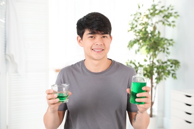 Photo of Man holding bottle and glass with mouthwash in bathroom. Teeth care