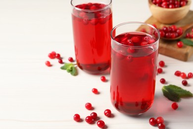 Photo of Tasty cranberry juice in glasses and fresh berries on white wooden table, closeup. Space for text