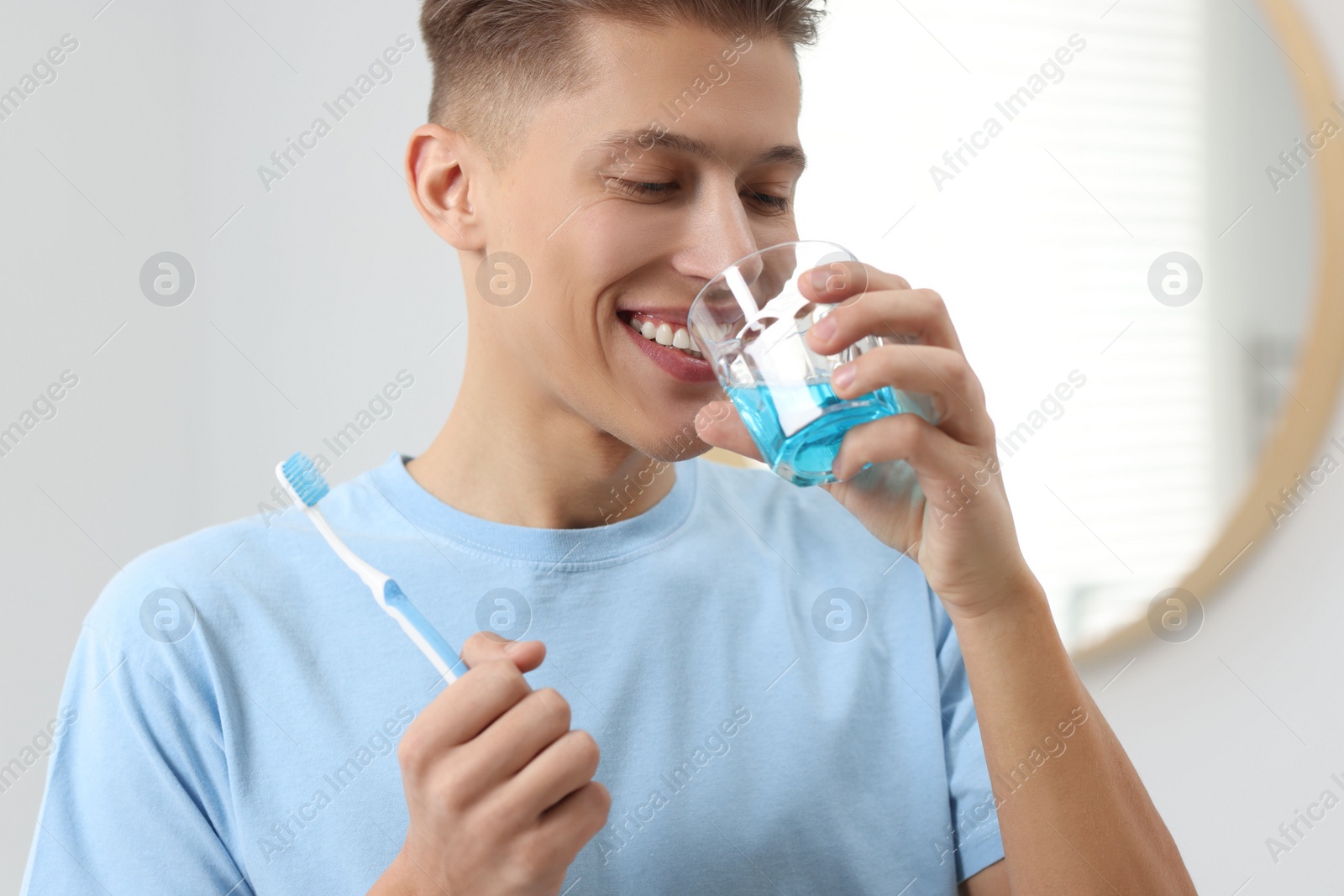 Photo of Young man using mouthwash in bathroom. Oral hygiene