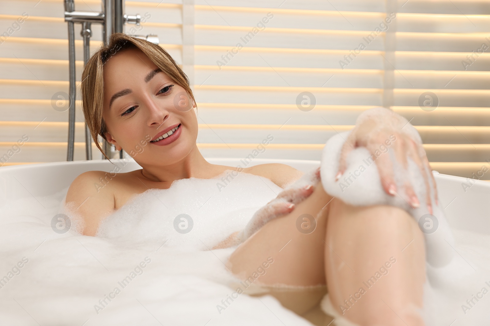 Photo of Happy woman taking bath with foam in tub indoors