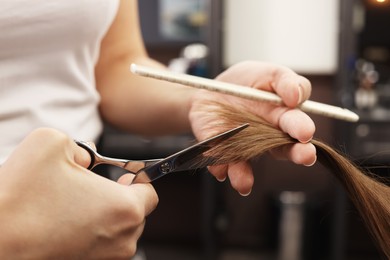 Professional hairdresser cutting woman's hair in salon, closeup