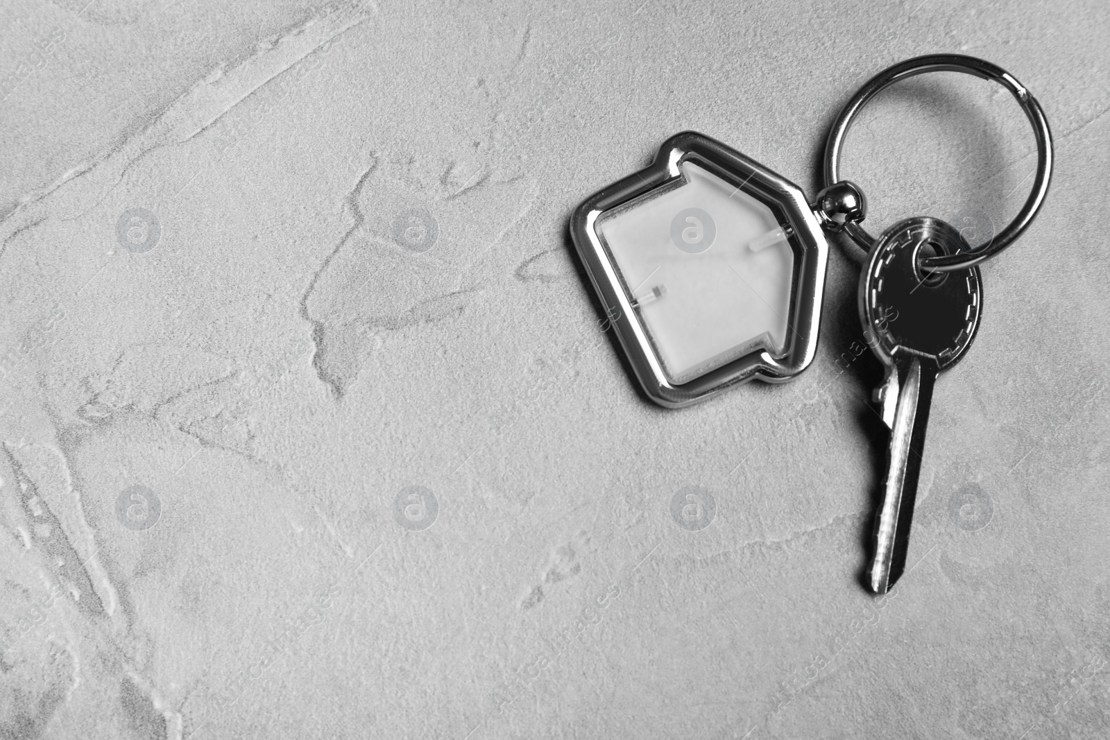 Photo of Key with trinket in shape of house on grey stone background, top view and space for text. Real estate agent services