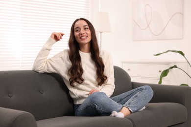 Photo of Beautiful young woman in stylish warm sweater on sofa at home