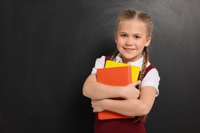 Photo of Happy schoolgirl with books near blackboard, space for text