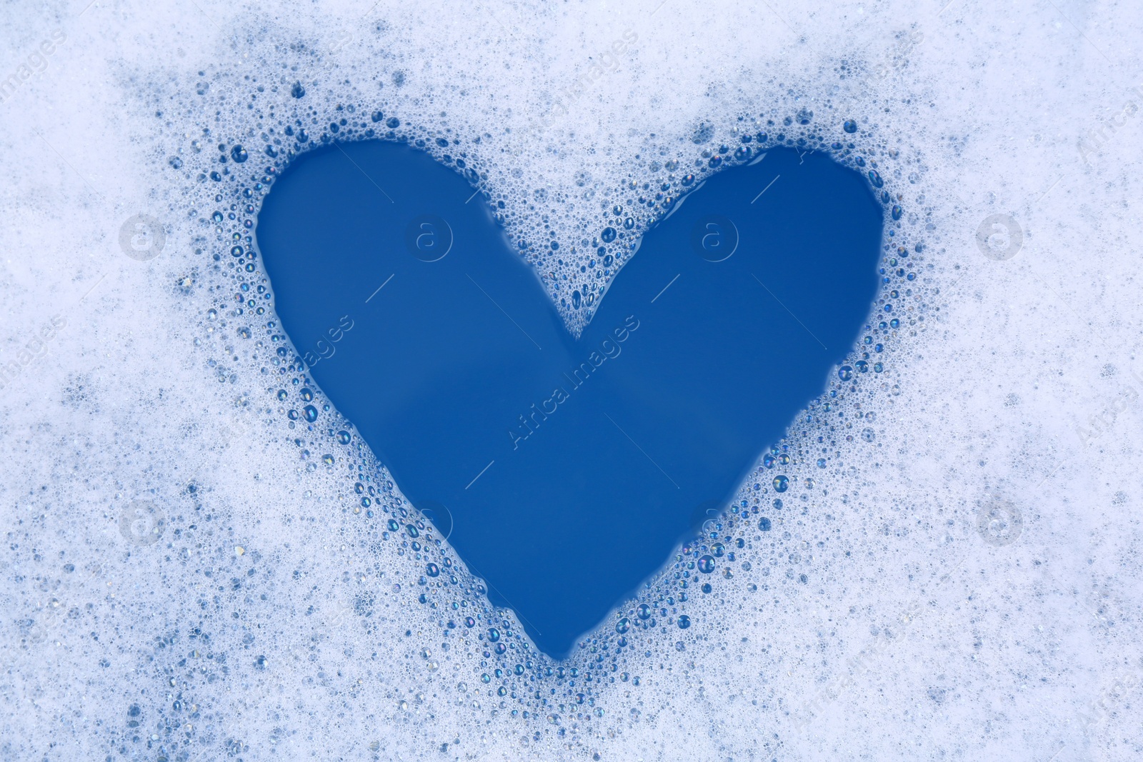 Photo of Heart shape made of detergent foam in water, top view. Hand washing laundry