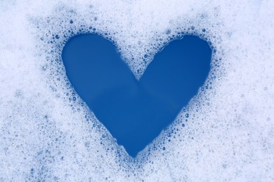 Photo of Heart shape made of detergent foam in water, top view. Hand washing laundry