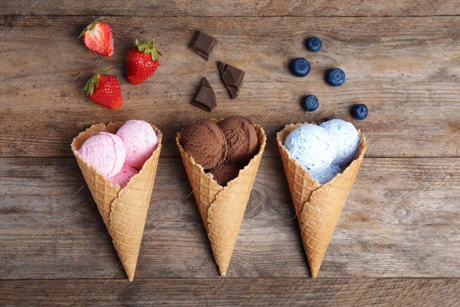 Photo of Flat lay composition with delicious ice creams in waffle cones on wooden table