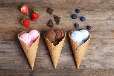 Flat lay composition with delicious ice creams in waffle cones on wooden table