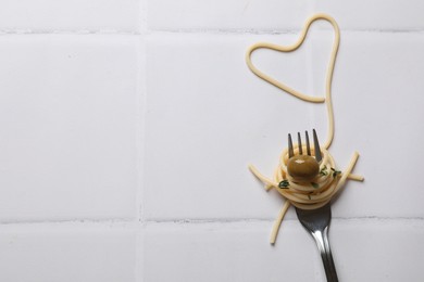 Photo of Heart made of tasty spaghetti, fork and olive on white tiled table, top view. Space for text