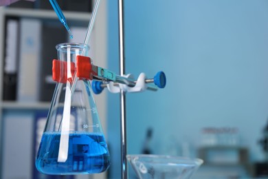 Laboratory analysis. Dripping blue liquid into flask on stand indoors, closeup. Space for text