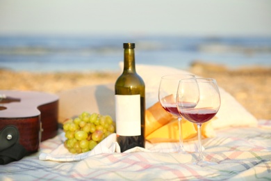 Photo of Blanket with food, wine and guitar on beach. Romantic picnic for couple