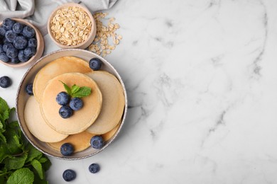 Photo of Tasty oatmeal pancakes with blueberries on white marble table, flat lay. Space for text