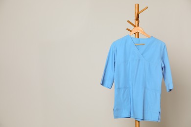Photo of Medical uniform hanging on rack against light grey background. Space for text