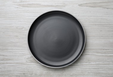 Photo of New dark plate on light wooden table, top view