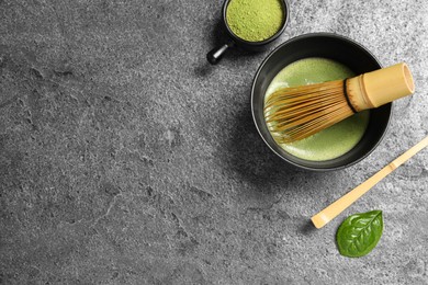 Photo of Cup of fresh matcha tea with bamboo whisk, spoon and green powder on grey table, flat lay. Space for text