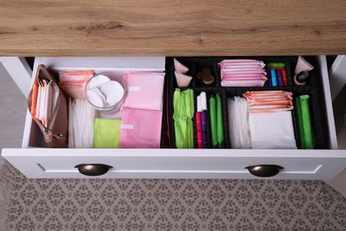 Photo of Open cabinet drawer with menstrual pads, tampons and skin care products indoors, above view