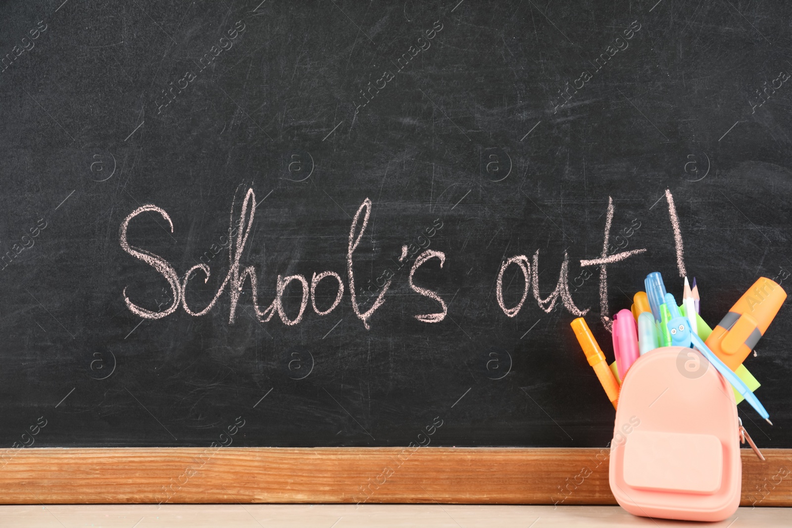 Photo of Stationery on table near blackboard with text School's Out. Summer holidays