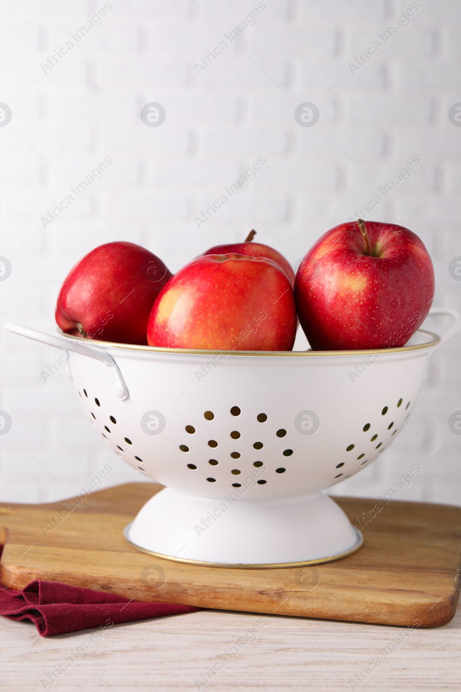 Photo of Fresh apples in colander on white wooden table