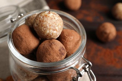 Photo of Different delicious vegan candy balls in glass jar on table, closeup