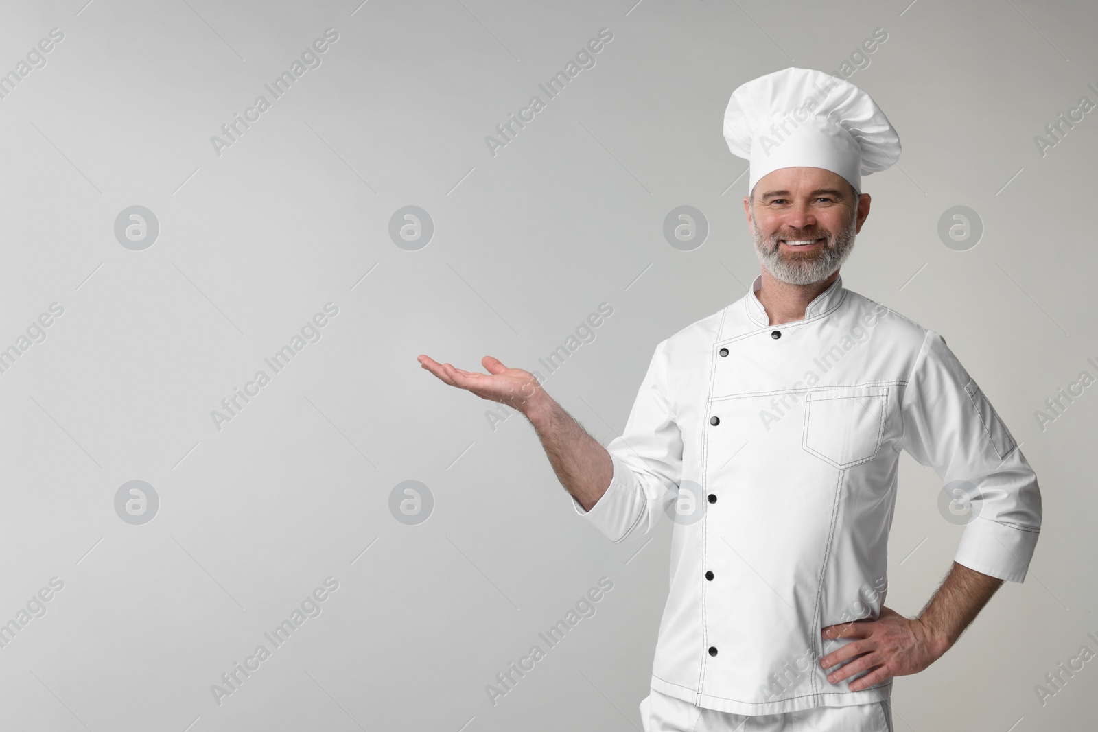 Photo of Happy chef in uniform posing on grey background, space for text