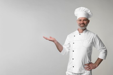 Photo of Happy chef in uniform posing on grey background, space for text